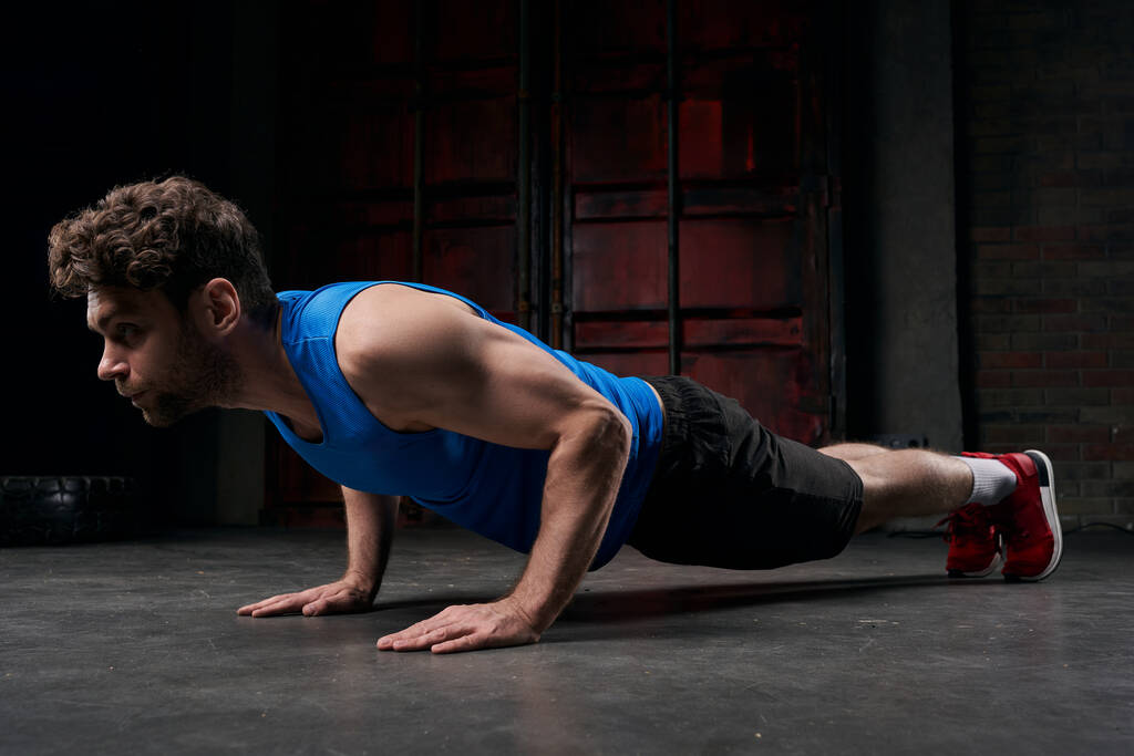 concentrated man in blue tank top training in plank pose in darkness of night urban street - Photo, Image