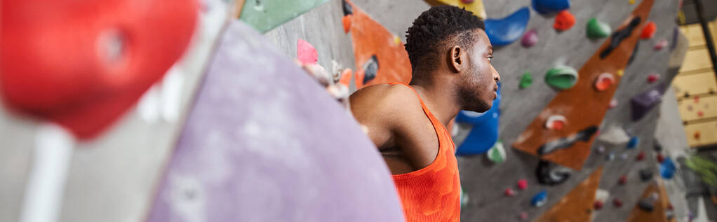 красивий афроамериканський чоловік в помаранчевій сорочці біля скелелазіння стіни дивиться геть, банер - Фото, зображення