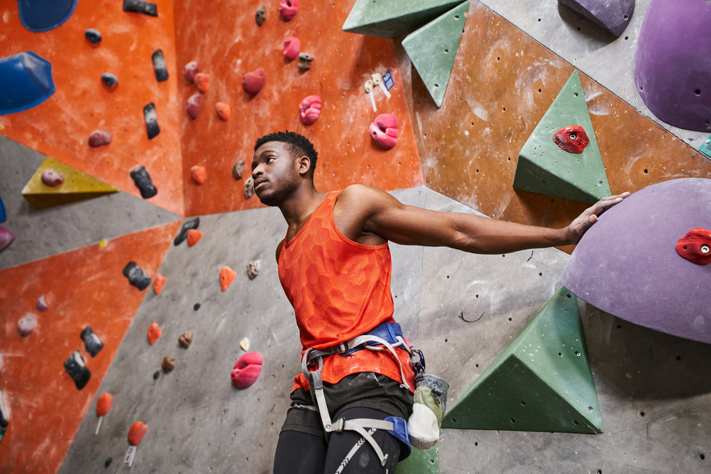 good looking african american man with alpine harness posing near climbing wall and looking away - Photo, Image