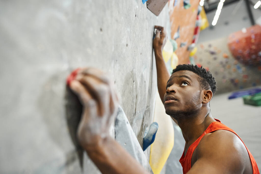 εμφανίσιμος νεαρός Αφροαμερικάνος σκαρφαλώνει στον τοίχο και κοιτάζει ψηλά, αθληταρά. - Φωτογραφία, εικόνα