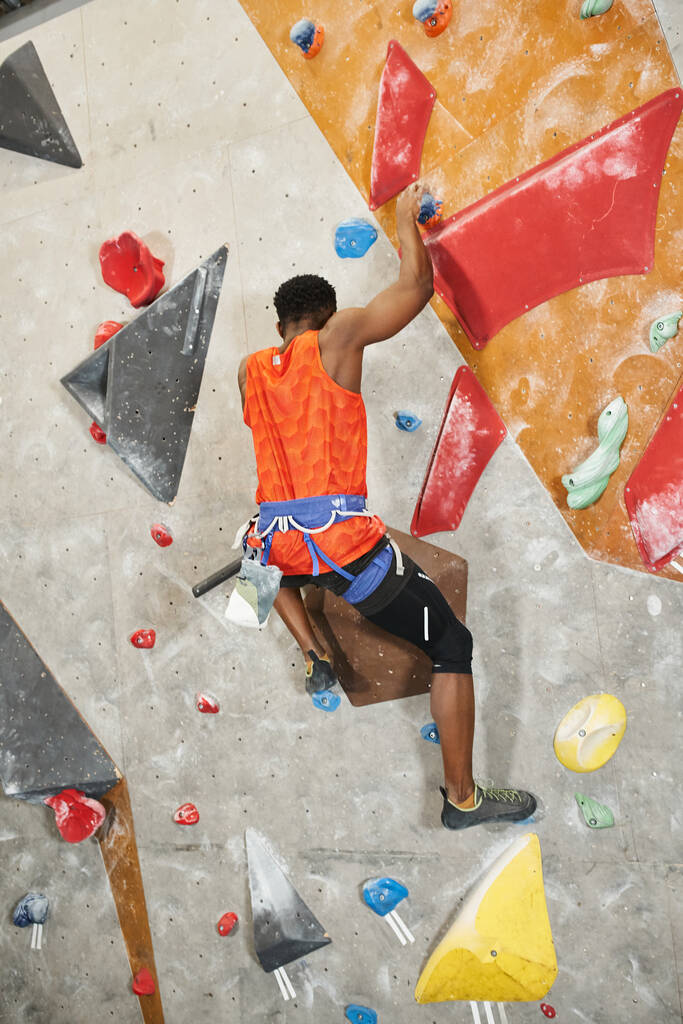 vertical shot of young african american man climbing up rock wall, back view, bouldering concept - Photo, Image
