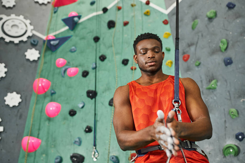 bell'uomo africano americano in camicia arancione con talco in polvere prima di arrampicarsi sulla parete rocciosa - Foto, immagini