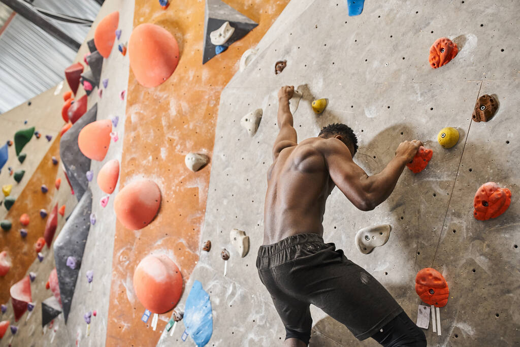 good looking fit african american man with his shirt off climbing up rock wall and looking down - Photo, Image