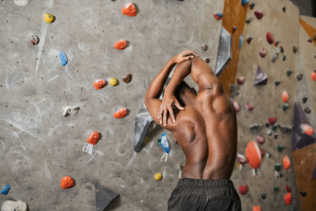 Rückenansicht des sportlichen, hemdslosen Afroamerikaners, der seinen Körper leicht beugt und die Muskeln spielen lässt - Foto, Bild