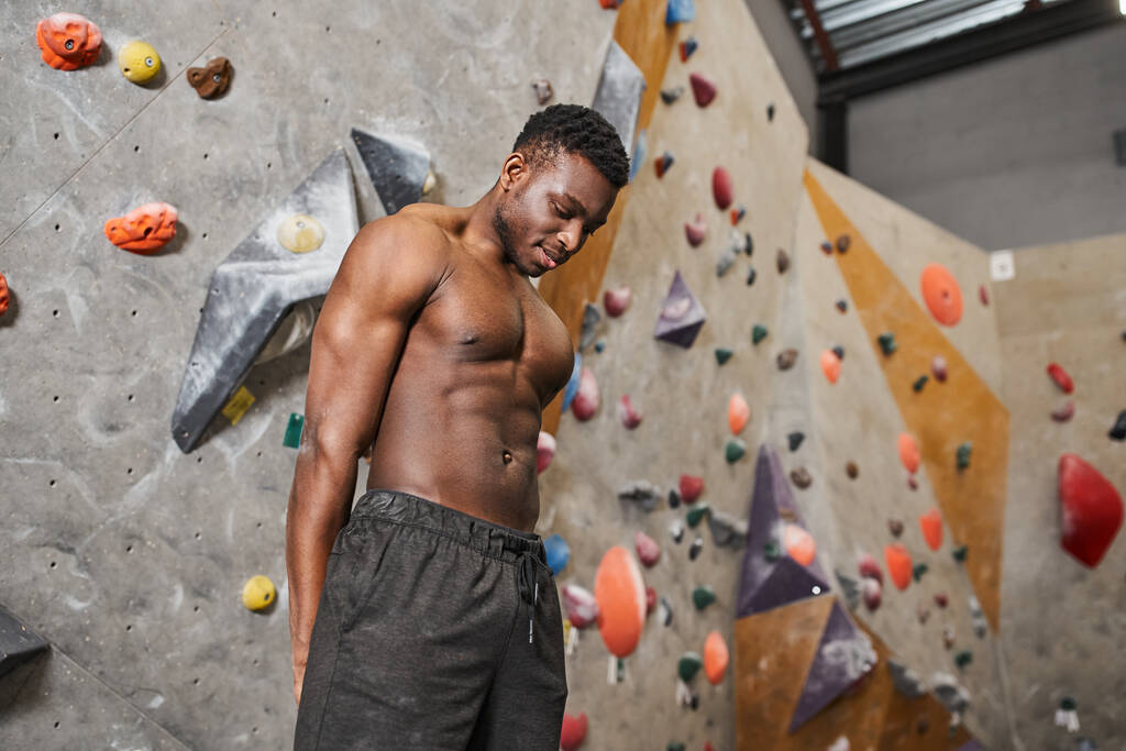 fröhlicher muskulöser afrikanisch-amerikanischer Mann in schwarzer Hose posiert oben ohne neben einer Boulderwand - Foto, Bild