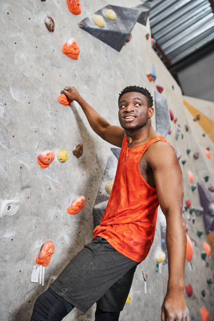 壁に登りながら喜んで遠ざかって笑っている強いアフリカ系アメリカ人男性の垂直撮影 - 写真・画像