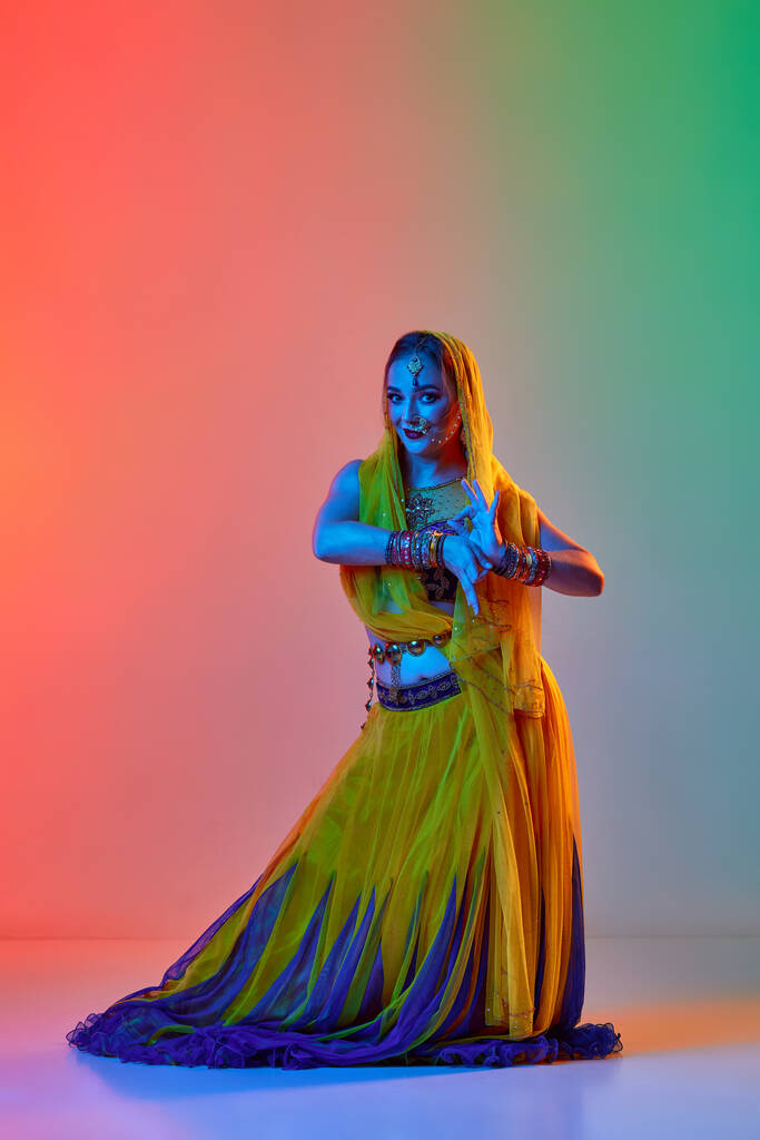 Танец Одисси. Красивая молодая женщина в традиционном платье танцует на фоне градиентной студии в неоновом свете. Концепция красоты, моды, Индии, традиций, образа жизни, хореографии, искусства. Объявление - Фото, изображение