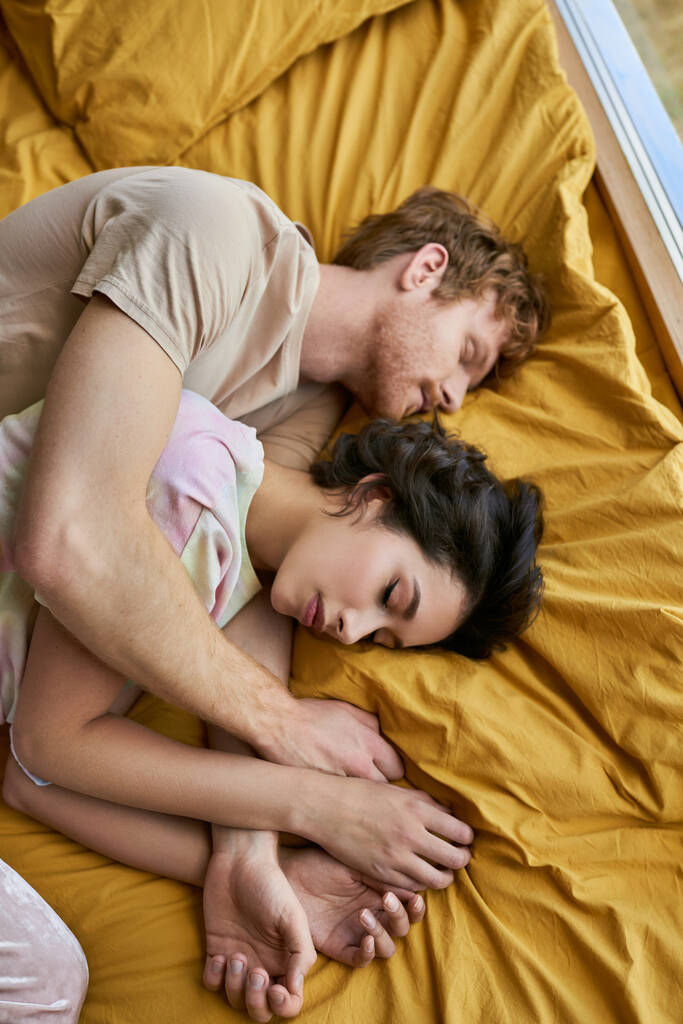 вид сверху на межрасовую пару, спящую вместе на уютном желтом постельном белье дома, утреннее время - Фото, изображение