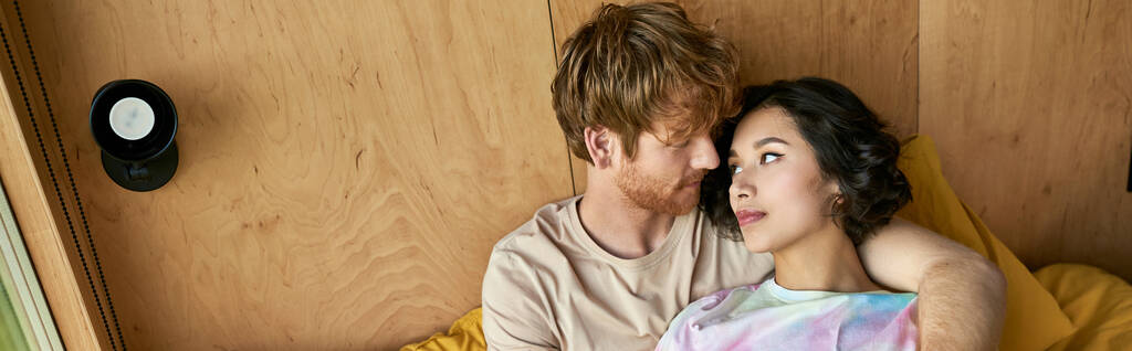 rousse homme embrassant jolie femme asiatique et couché sur le lit près de la fenêtre dans la maison de campagne, bannière - Photo, image