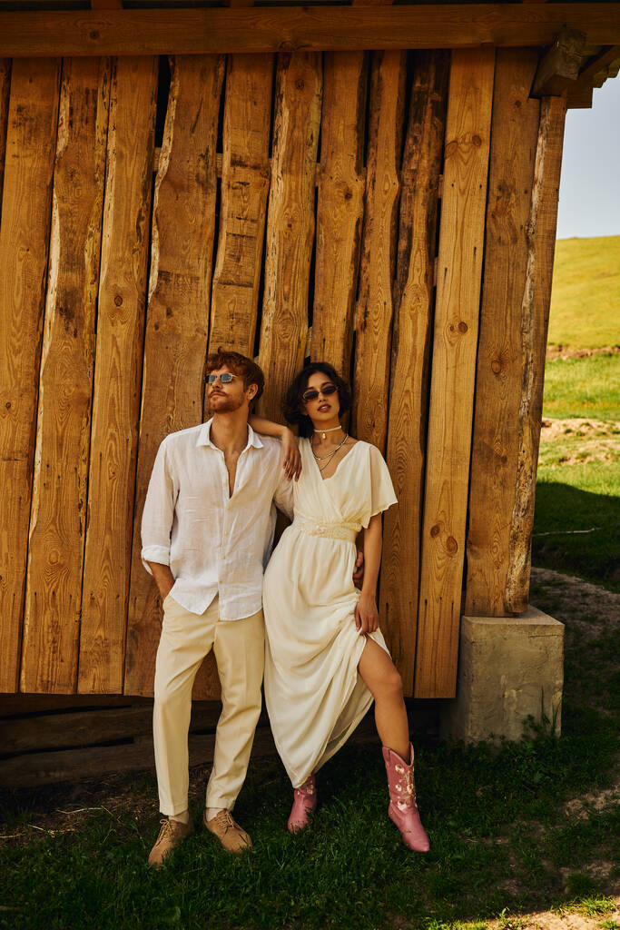 rustic wedding in boho style, stylish asian bride in wedding dress standing with groom in sunglasses - Photo, Image