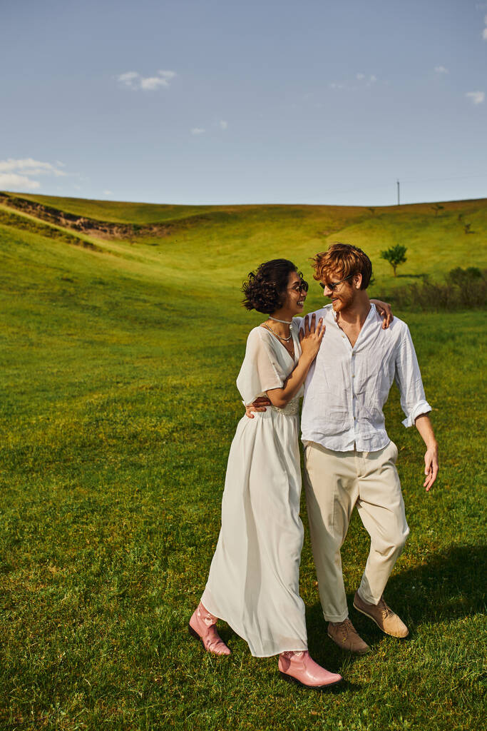 молодожены, невеста в белом платье, гуляющая с грумом по полю, сельской природе - Фото, изображение