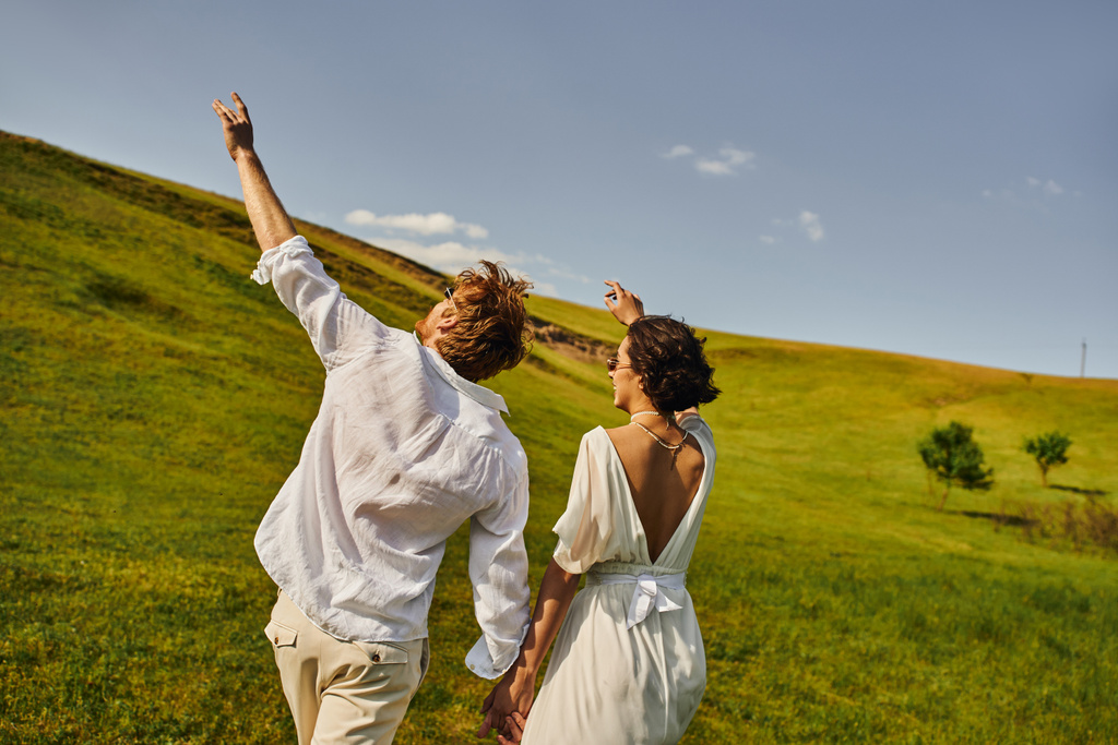 mariage rural, couple marié en robe de mariée tenant la main et marchant dans le champ vert - Photo, image
