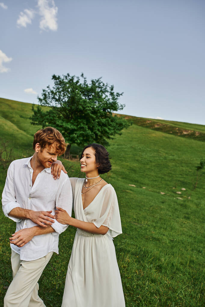 сільська природа, щасливі молодята у весільній сукні, що йдуть разом у зеленому полі, просто подружня пара - Фото, зображення