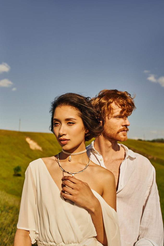 charming asian woman in boho style wedding dress near young redhead groom in scenic rural setting - Photo, Image