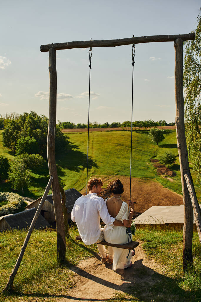 casamento rústico, vista para trás de jovens recém-casados em swing no campo com paisagem cênica verde - Foto, Imagem