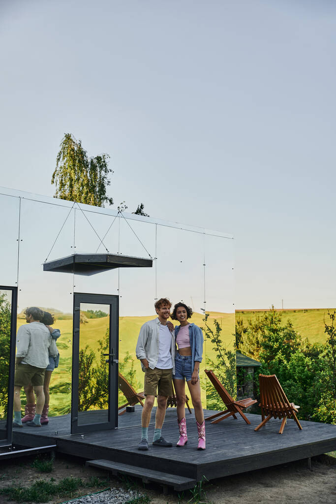 plná délka šťastný mezirasový pár dívá pryč na verandu moderního skleněného domu na venkově - Fotografie, Obrázek