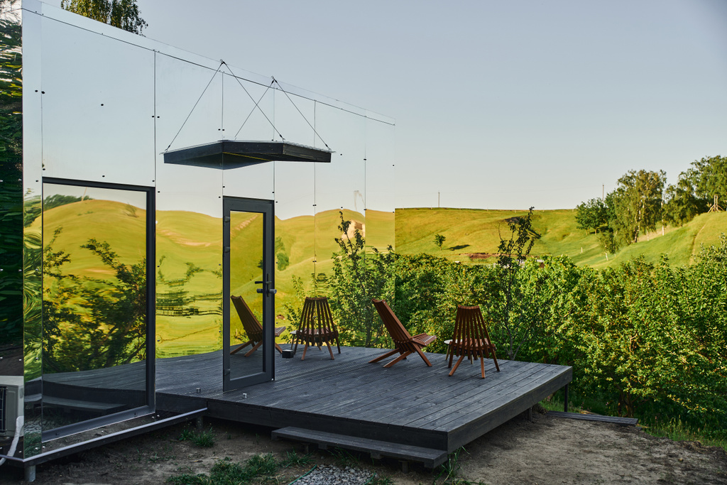 ekologiczny szklany dom z krzesłami na drewnianej werandzie i widokiem na malowniczy krajobraz wiejski - Zdjęcie, obraz