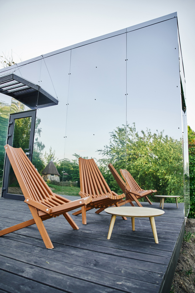 Holzstuhl und Couchtisch in der Nähe eines modernen umweltfreundlichen Glashauses in ruhiger ländlicher Umgebung - Foto, Bild