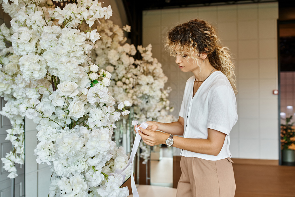 fleuriste créatif avec ruban blanc arrangeant décor floral blanc dans la salle de banquet pour une occasion spéciale - Photo, image