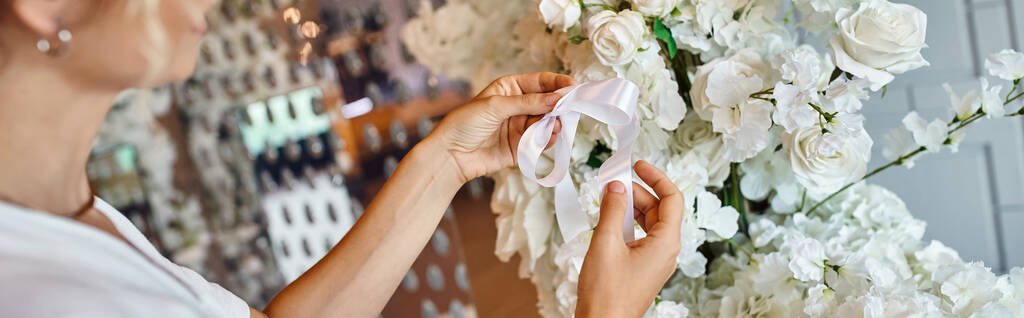 bijgesneden weergave van decorateur koppellint op witte bloemen samenstelling in feestelijke evenementenhal, banner - Foto, afbeelding