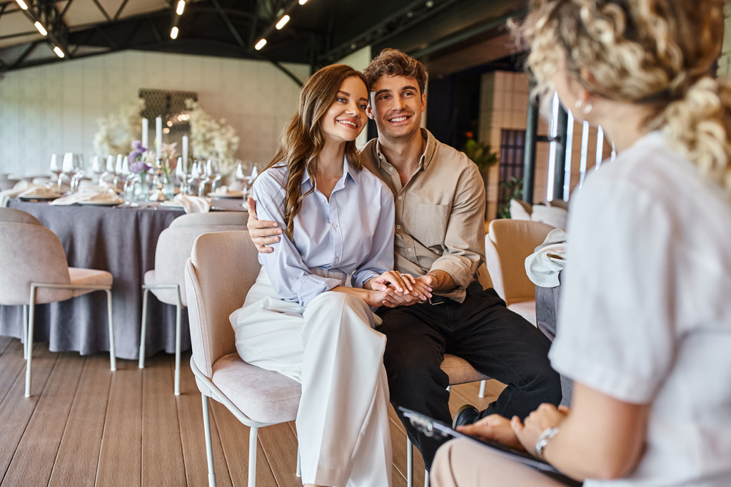šťastný pár při pohledu na rozmazané události manažer při sezení u slavnostního stolu ve svatební síni - Fotografie, Obrázek