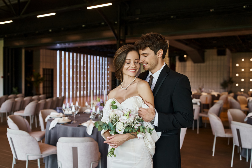 encantado casal em traje de casamento elegante sorrindo para a câmera no salão de banquetes moderno, banner - Foto, Imagem
