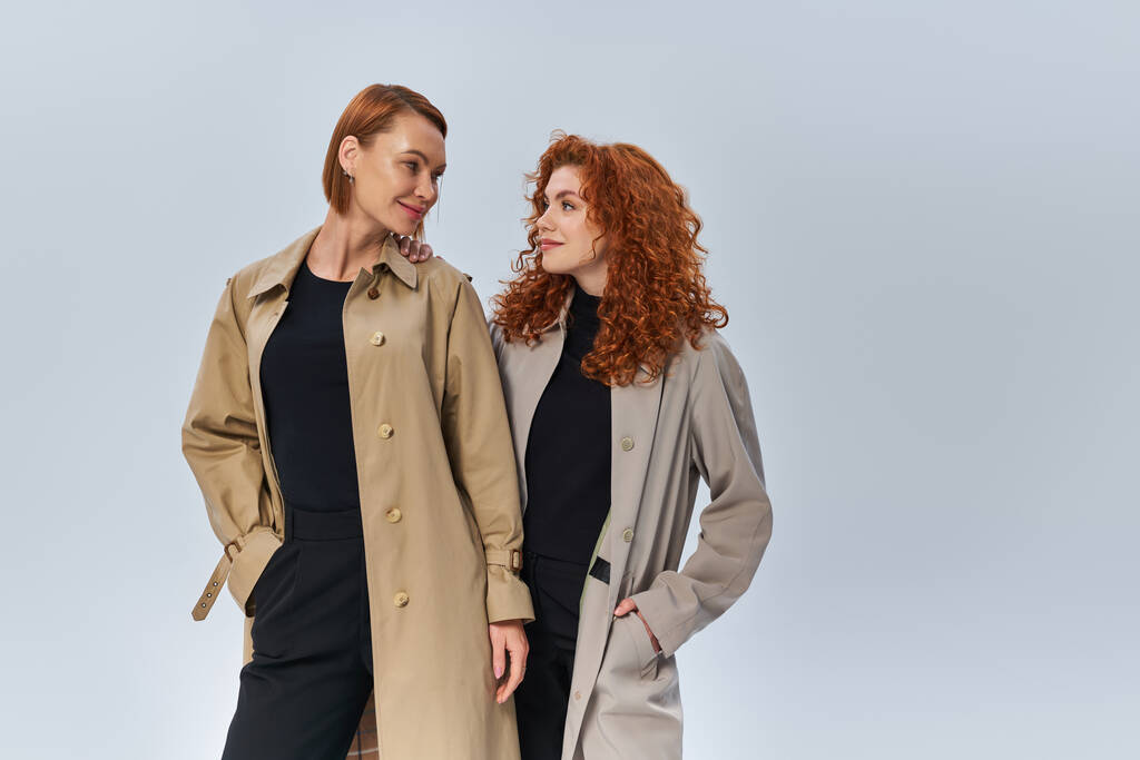 duas gerações de mulheres ruivas posando em casacos e olhando umas para as outras em fundo cinza - Foto, Imagem