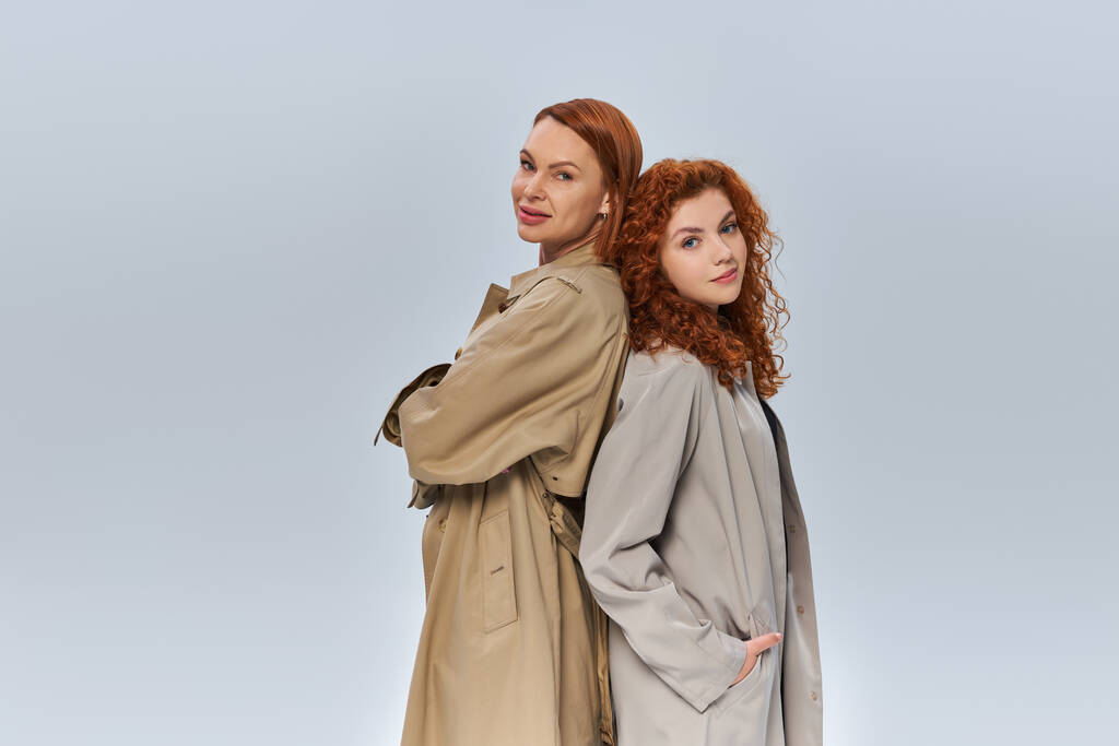 duas gerações de mulheres ruivas posando em casacos de trincheira outonal em fundo cinza, traje sazonal - Foto, Imagem