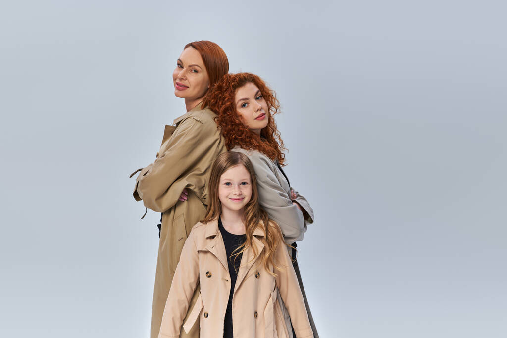 κοκκινομάλλα στέκεται κοντά ευτυχείς συγγενείς σε παλτό σε γκρι φόντο, γυναικεία γενιά, φθινοπωρινό στυλ - Φωτογραφία, εικόνα
