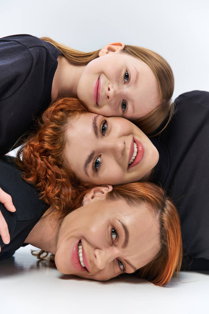 Drei Generationen Konzept, glückliche Frauen und Mädchen lächelnd und vor grauem Hintergrund in die Kamera blickend - Foto, Bild