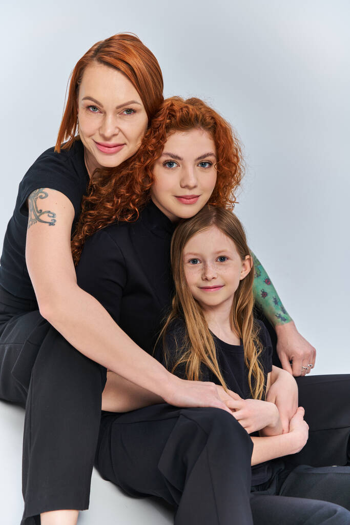 concetto di tre generazioni, gioiosa famiglia rossa in abiti coordinati che si abbracciano su sfondo grigio - Foto, immagini