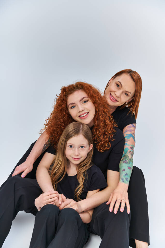 glückliche Familie mit roten Haaren in passenden Outfits vor grauem Hintergrund, drei Generationen - Foto, Bild