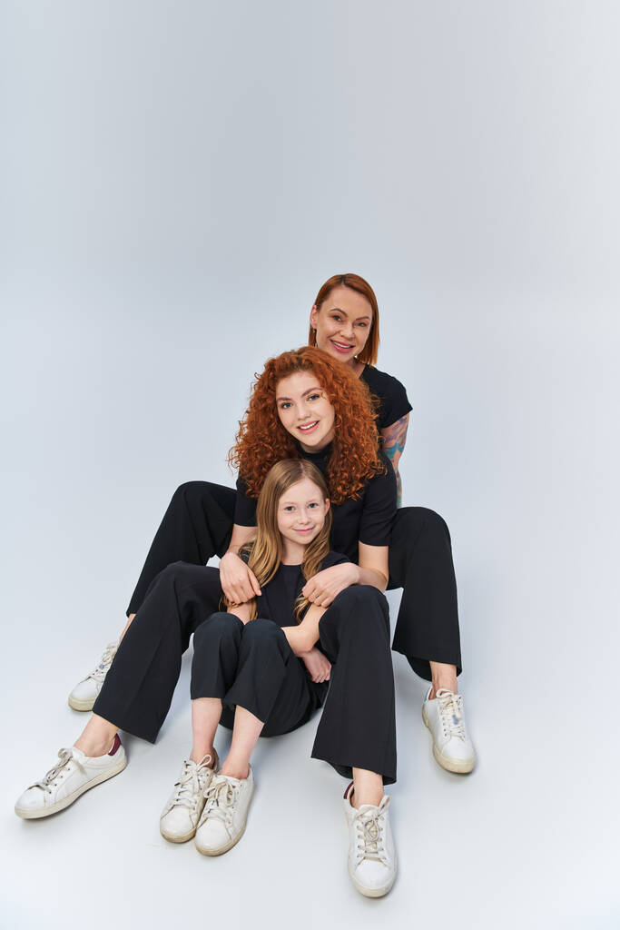 redhead family in matching outfits hugging and sitting together on grey backdrop, three generations - Photo, Image