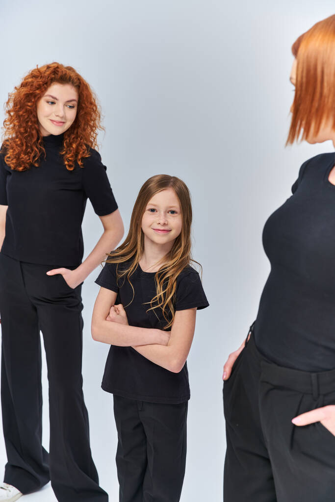 happy girl standing with folded arms near redhead family in matching clothes on grey backdrop - Photo, Image