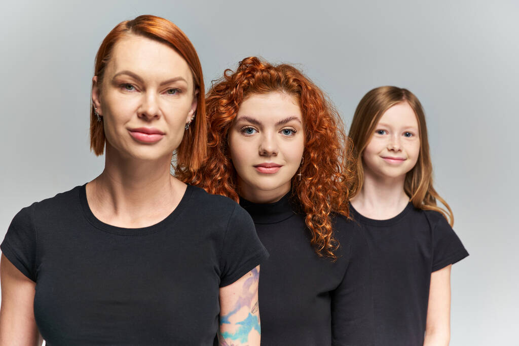 τρεις γενιές κοκκινομάλλων γυναικών και παιδιών που ποζάρουν με ασορτί ενδυμασία σε γκρι φόντο, οικογένεια - Φωτογραφία, εικόνα