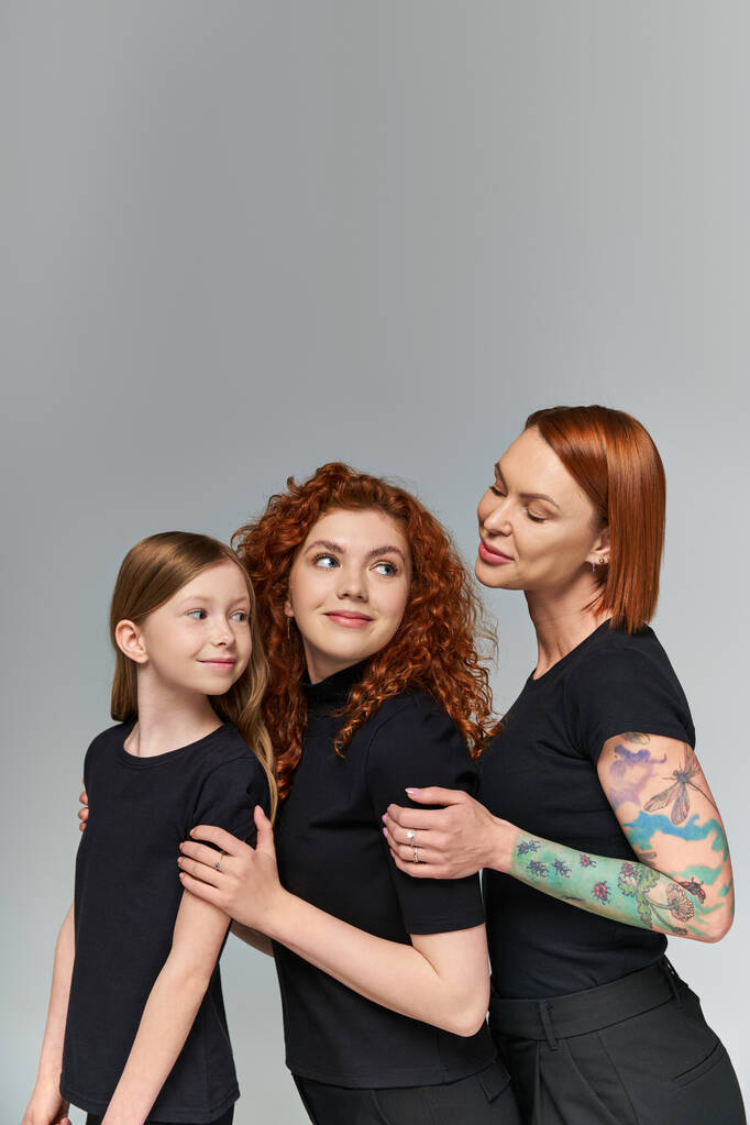 három generáció koncepció, vidám vörös hajú nők és a lány megfelelő öltözékben ölelés szürke háttér - Fotó, kép