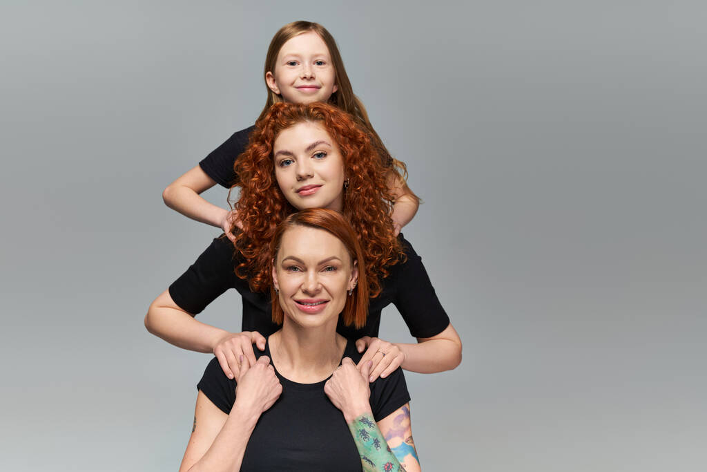 női generáció koncepció, boldog vörös hajú család megfelelő öltözékben ölelés szürke háttér - Fotó, kép