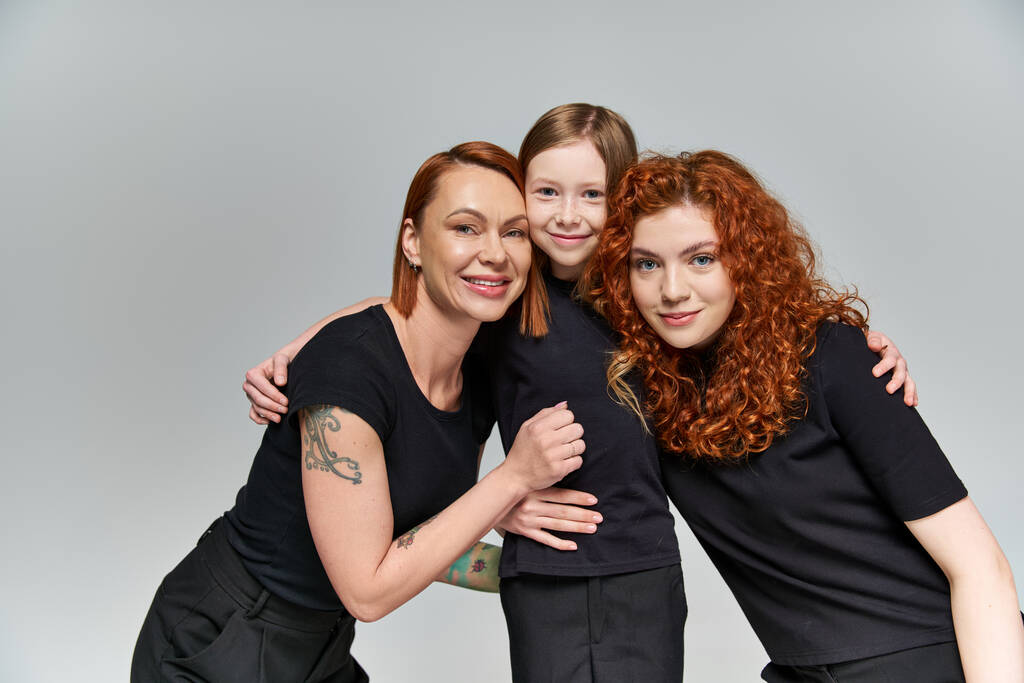 Familienporträt, glückliches sommersprossiges Mädchen umarmt rothaarige Familie in passender Kleidung auf grauem Hintergrund - Foto, Bild