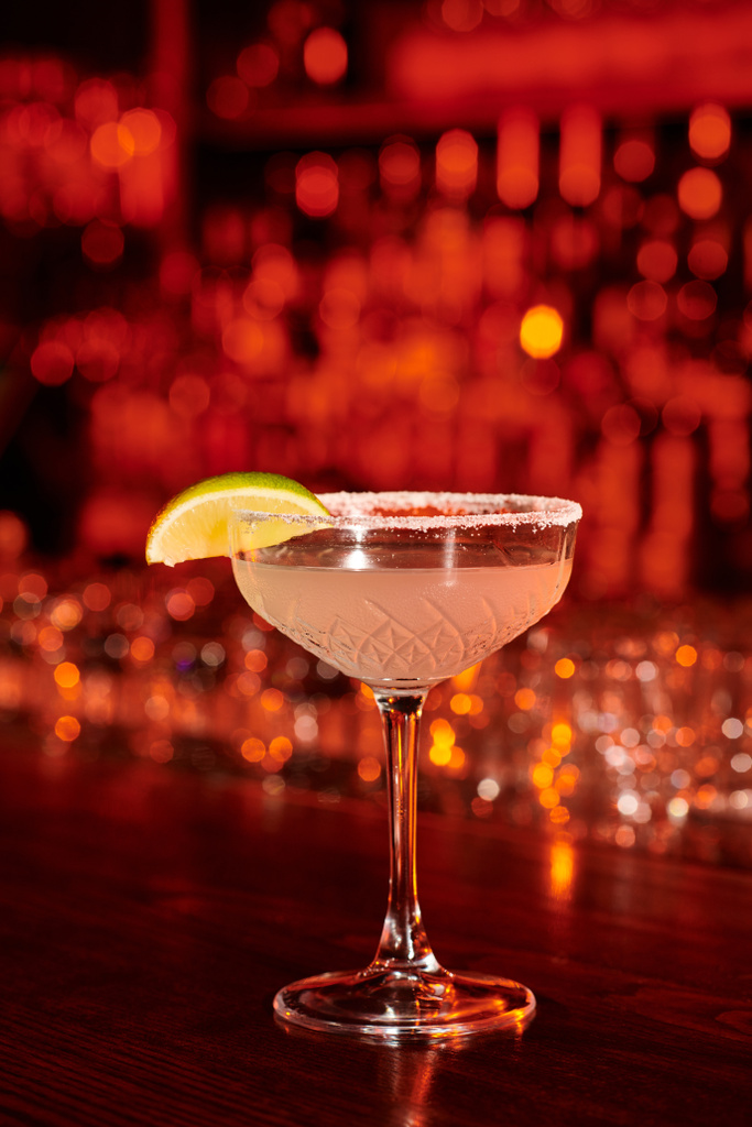 изысканный коктейль Маргарита украшенный ломтиком лайма и льдом на барной стойке, концепция - Фото, изображение