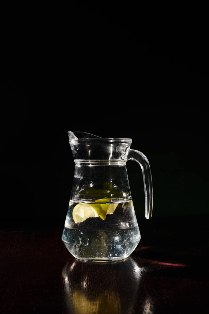 τεράστια δίψα σβήσιμο και φρέσκο κανάτα με καθαρό νερό με μικρές φέτες λεμονιού σε μαύρο φόντο - Φωτογραφία, εικόνα