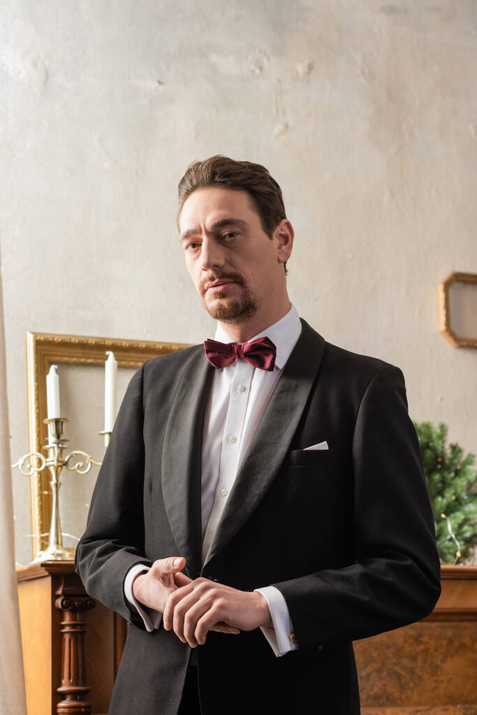 zamożny dżentelmen w formalnym stroju z muszką stojący w pobliżu fortepianu w Wigilię, święto - Zdjęcie, obraz