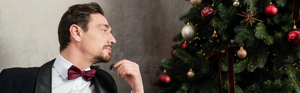 caballero bien vestido con barba usando esmoquin con pajarita mirando el árbol de Navidad, pancarta - Foto, Imagen