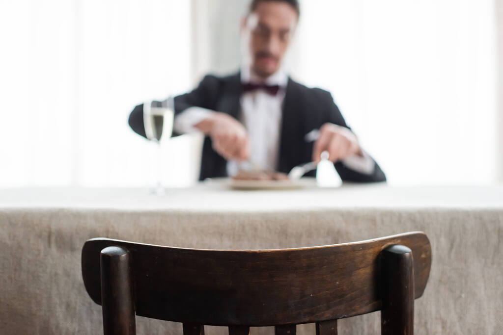 focus on wooden chair, wealthy gentleman in tuxedo enjoying dinner at home, natural light - Photo, Image