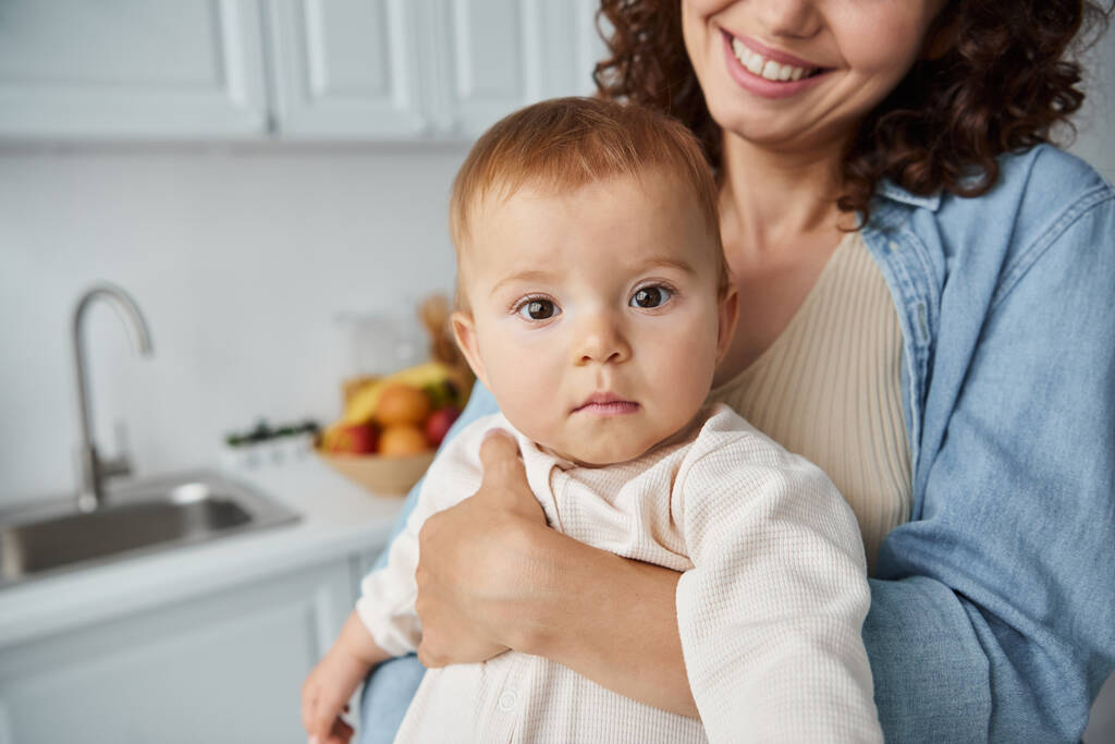portrait of adorable baby girl in hands of joyful mother in kitchen at home, happy childhood - Photo, Image