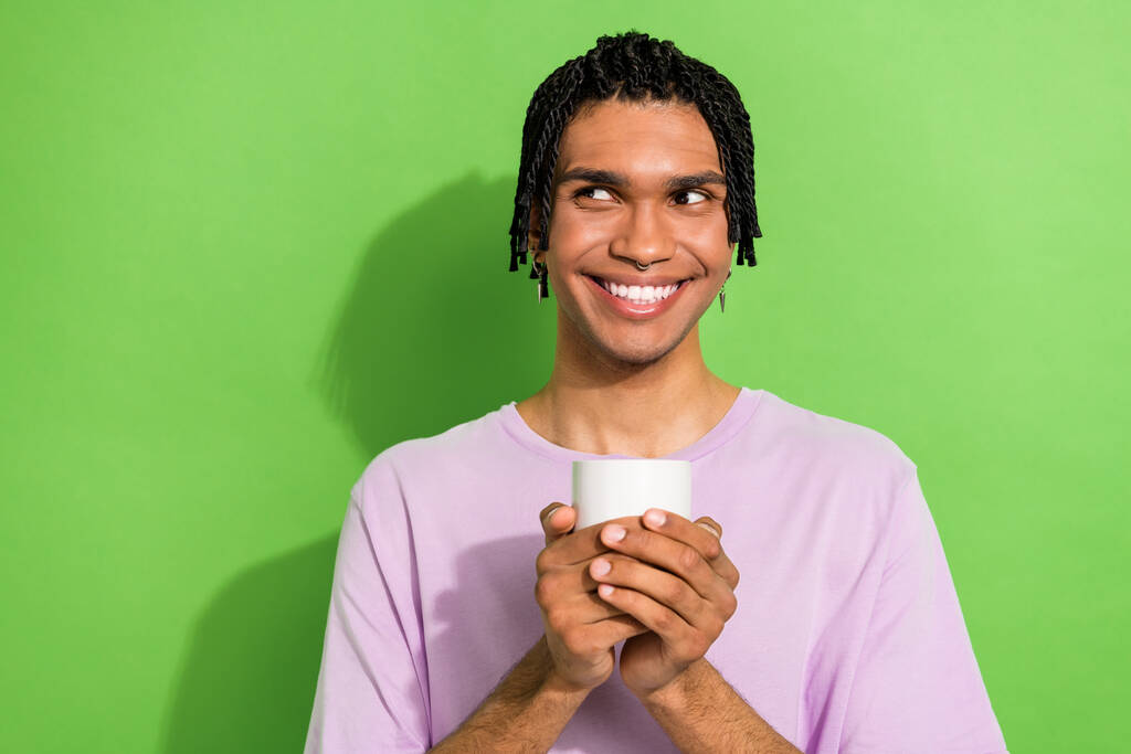Foto von nett gesinnten kreativen Mann zahmes Lächeln halten Kaffeetasse suchen leeren Raum isoliert auf grünem Hintergrund. - Foto, Bild