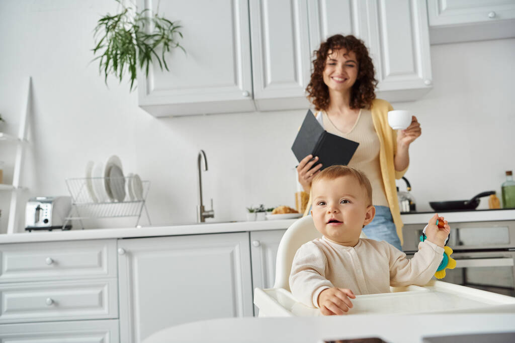 lapsi leikkii helistin lelu lähellä äiti kannettavan ja kahvikupin moderni keittiö - Valokuva, kuva