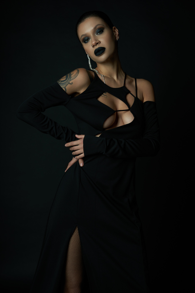Tätowierte Frau in dunklem Make-up und sexy Halloween-Kleid im dunklen Studio vor der Kamera, schwarze Magie - Foto, Bild