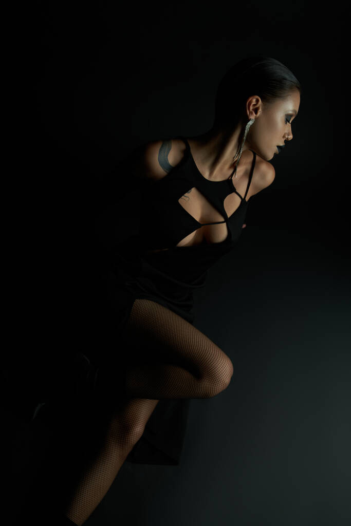 hoge hoek uitzicht van sexy vrouw in halloween jurk zitten met gesloten ogen op zwarte achtergrond - Foto, afbeelding