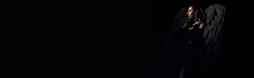 vue latérale de la femme en costume d'ange déchu priant sur fond noir, beauté démoniaque, bannière - Photo, image