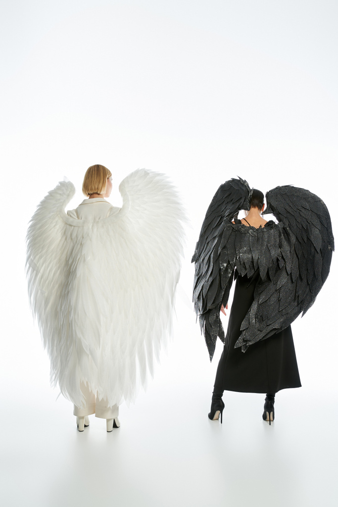 widok z tyłu kobiety w kostiumach diabła i anioła z czarnymi i jasnymi skrzydłami na białym, pełnej długości - Zdjęcie, obraz